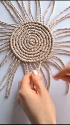 two hands are working on an art project with rope and yarn, which looks like a sunflower