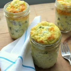 three small jars filled with food on top of a wooden table next to a fork