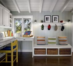 a room with white walls and wooden floors has two benches, a desk, and several baskets on the wall