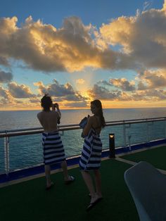 two people standing on the deck of a cruise ship watching the sun set over the ocean