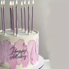 a birthday cake with pink frosting and lit candles on it that says happy birthday