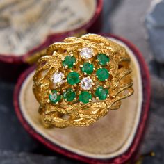 an ornate gold ring with emeralds and diamonds in a red velvet box on display