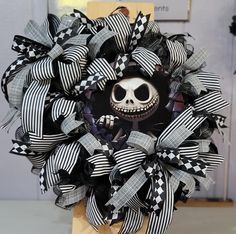 a black and white wreath with a skeleton face on the front, sitting on top of a wooden stand