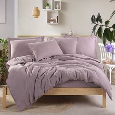 a bed with purple comforter and pillows in a room next to a potted plant