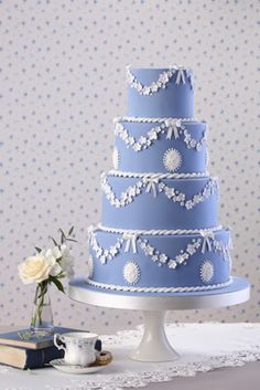 a blue wedding cake sitting on top of a table next to a vase with flowers