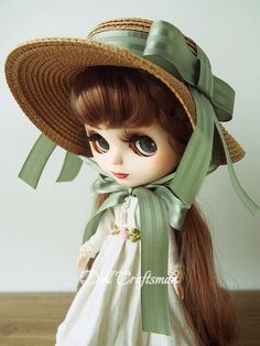 a doll with long hair wearing a hat and green ribbon around it's neck