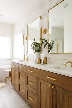 a bathroom with two sinks, mirrors and gold handles on the vanity tops in front of a bathtub