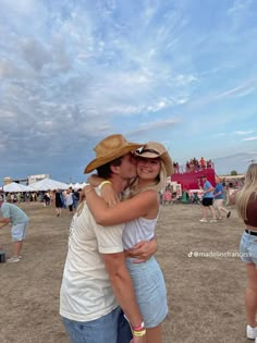 two people hugging each other in the middle of an open field with many people standing around