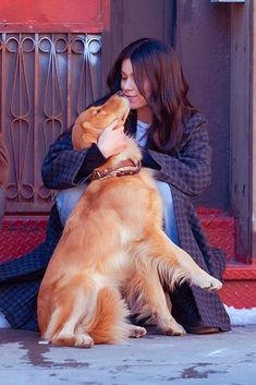 a woman sitting on the ground with her dog and petting it's face