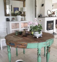 an old table with flowers on it in a living room next to a fire place