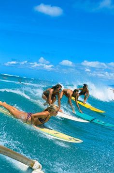 four surfers are riding the waves on their surfboards in the blue sky and white clouds