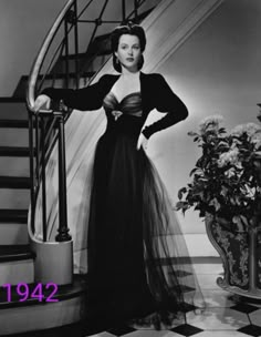 an old photo of a woman in a long dress standing on the stairs with her hands on her hips