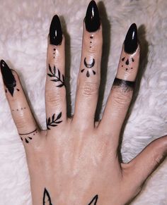 a woman's hand with black nail polish and tattoos on her fingers, which are decorated with leaves