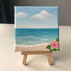 an easel with a painting on it sitting on a table next to the ocean