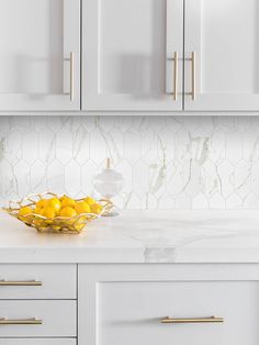 a bowl filled with lemons sitting on top of a counter next to white cabinets