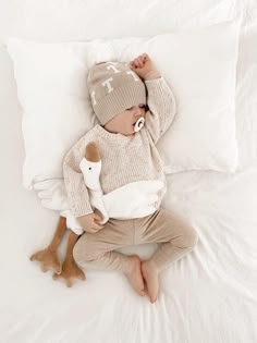 a baby laying on top of a bed wearing a hat and holding a stuffed animal