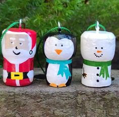 three snowman, penguin and santa candle holders sitting on a stone wall next to some plants