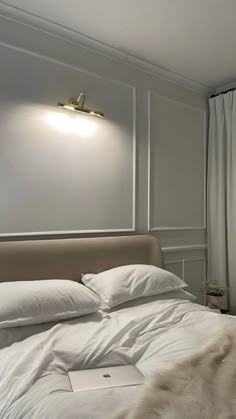 a bed with white linens and pillows in a bedroom next to a window that has drapes on it