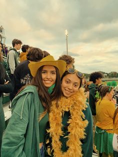 two girls dressed in green and yellow are posing for the camera at a football game