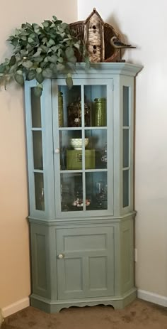 a blue china cabinet with glass doors and plants on top