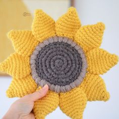 a hand holding up a knitted sunflower ornament in yellow and grey