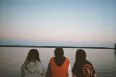 three people standing on the edge of a body of water looking at something in the distance