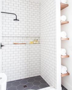 a white tiled bathroom with wooden shelves and towels on the shelf next to the shower