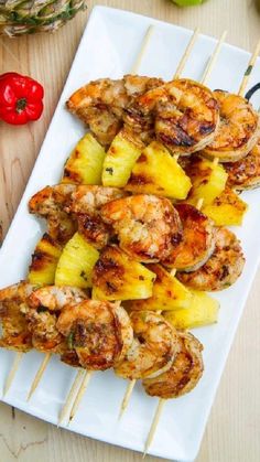 grilled shrimp and pineapple skewers on a white plate with red peppers