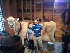 two boys standing next to a cow in a barn