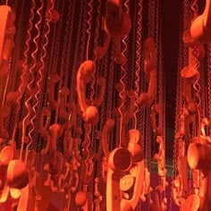 an array of telephones hanging from chains in a room with red lights on the ceiling