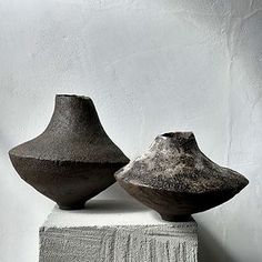 two black vases sitting on top of a white block in front of a wall