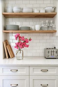 a white kitchen with open shelving and pink flowers in a vase on the counter