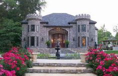 a stone house with pink flowers in the front yard and steps leading up to it