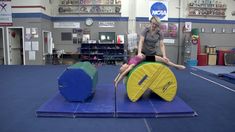 a woman is doing an acrobatic trick on a mat in a gym