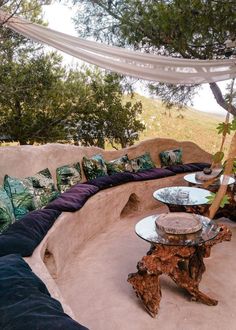 an outdoor seating area with couches, tables and pillows on the outside wall next to trees