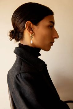 a woman with a black coat and earrings on her head, looking off to the side