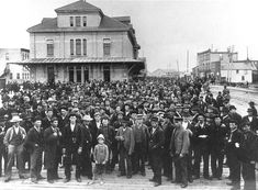 a large group of people standing in front of a building on a boardwalk with buildings behind them