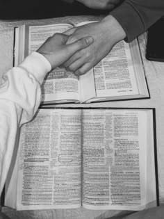 two people holding hands over an open book