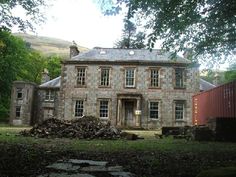 an old stone house in the middle of a wooded area with a train passing by