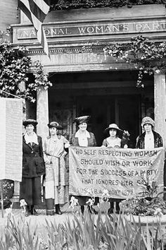 an old black and white photo of people holding a sign in front of a building