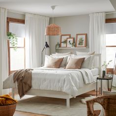 a white bed sitting in a bedroom next to two windows and a basket on the floor