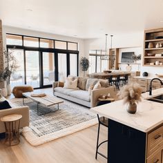 a living room filled with furniture next to a kitchen and dining room table in front of a large window