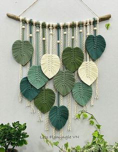 a green and white wall hanging with leaf shapes on it, next to a potted plant