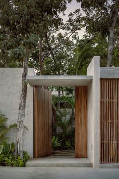 an entrance to a house surrounded by trees and bushes with wooden doors on either side