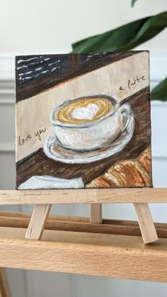 a painting of a cup of coffee on top of a wooden easel