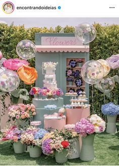 a table topped with lots of balloons and flowers in front of a flower shop display