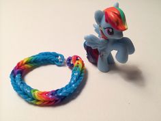 a little pony toy next to a rainbow braid bracelet on a white table with a small pony figure