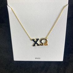 a necklace with the letter xo on it in gold and black, sitting on top of a white card