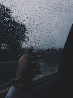 a person's hand is holding the handle of a car window as it rains