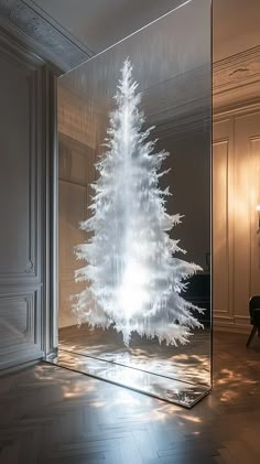 a white christmas tree is in a glass case on the floor next to a chair